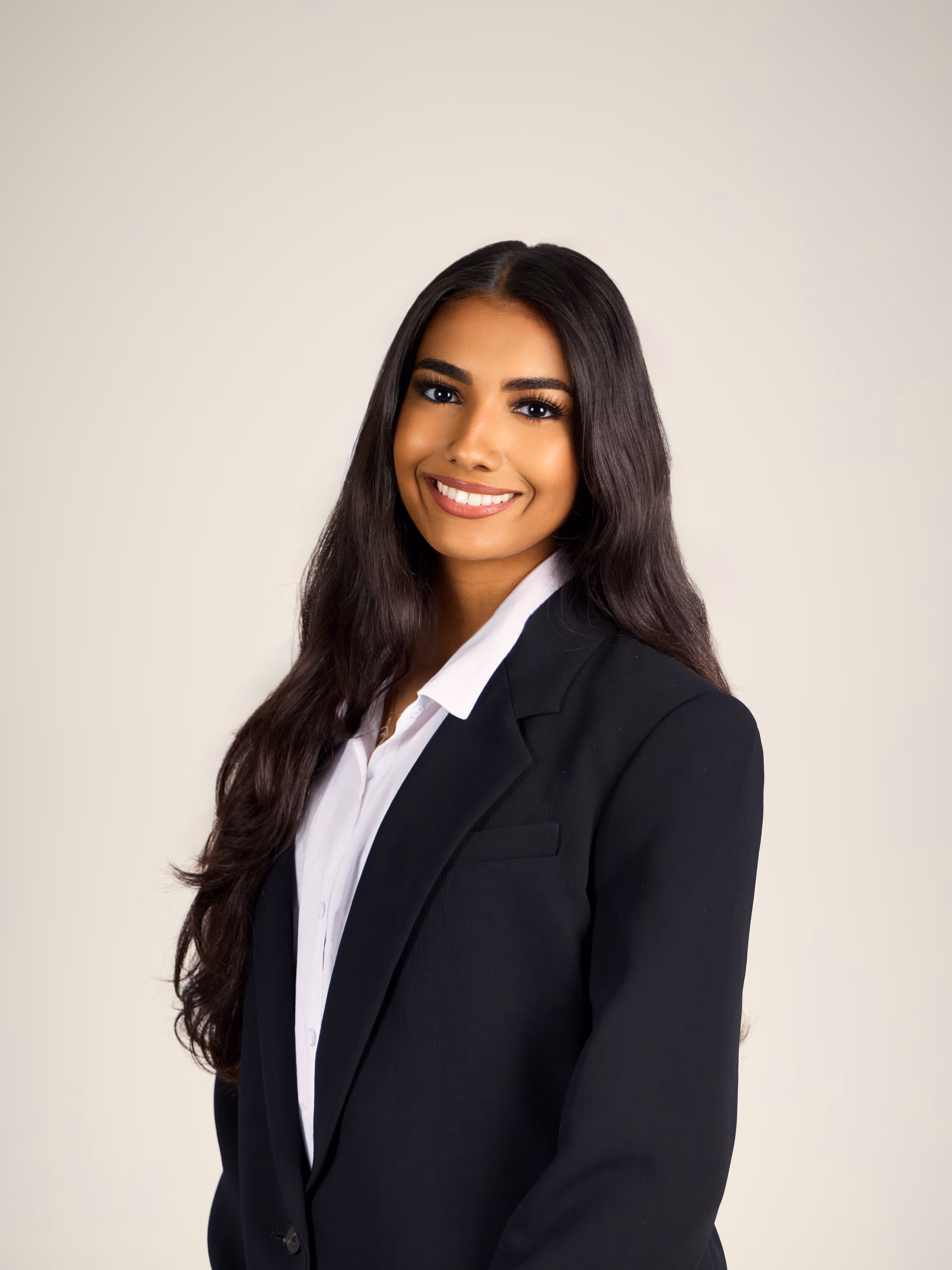 Sophia with long dark hair wearing a black blazer and white shirt smiling against a light background.